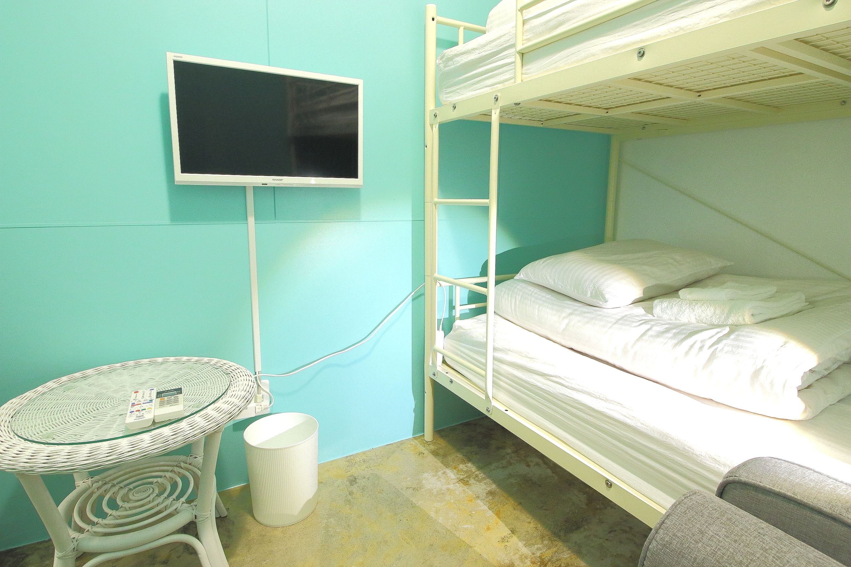 A bunk bed with white bedding, a small table with a glass top, and a television mounted on the wall.