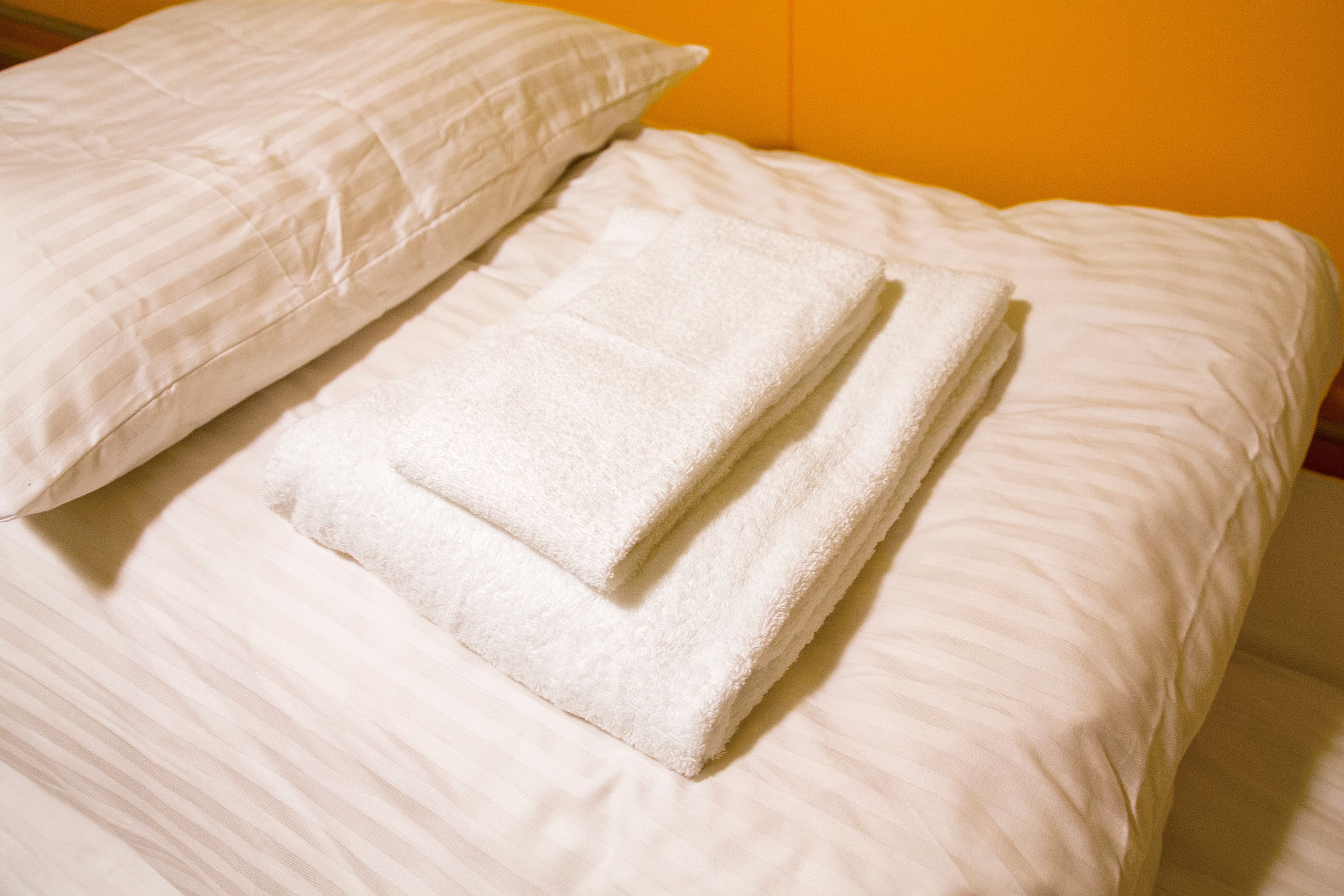 A neatly made bed with white linens and pillows, set against a plain background.