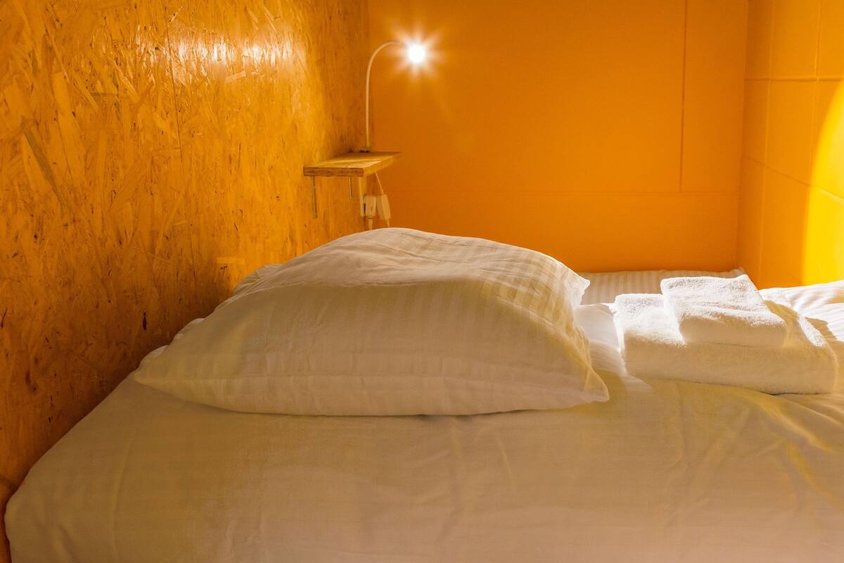 A bed with white linens in a room with wooden walls and a bright yellow accent wall.