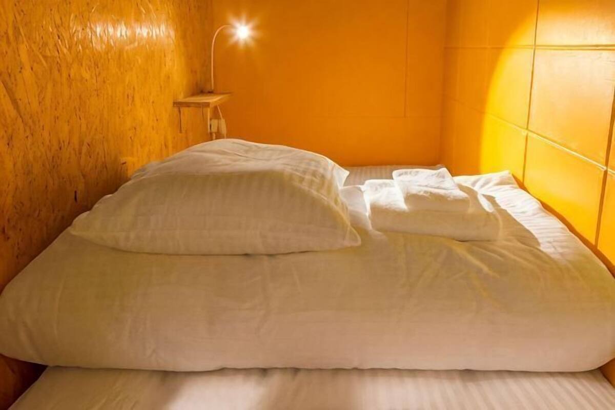 A bed with white bedding in a room with a wooden wall and a bedside lamp.