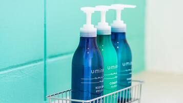 Three bottles of body soap in a metal basket against a teal wall.