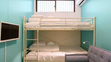 A bunk bed room with a television on the left, a window with blinds, and a chair in the foreground.