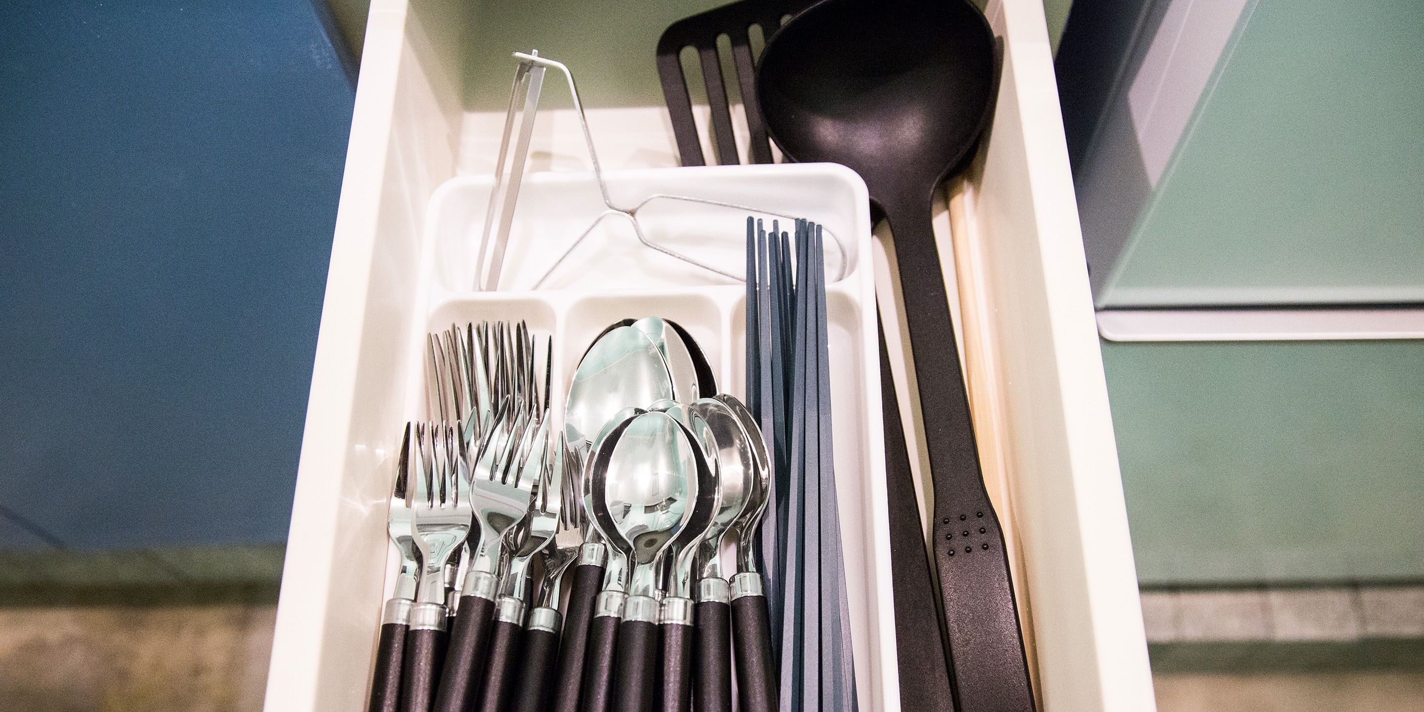 A drawer containing various utensils including forks, spoons, and a black spatula.