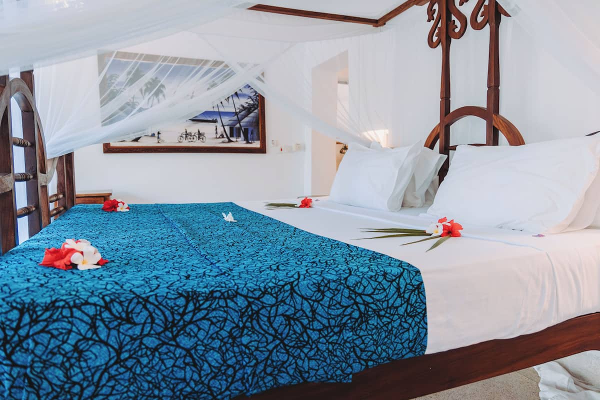 Una cama con dosel, con un edredón azul estampado, almohadas blancas y dosel.