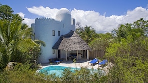 A white building with a thatched roof, a pool, and lounge chairs. - Shooting Star Boutique Hotel (Kiwengwa)