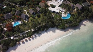 An aerial view of a tropical resort with multiple bungalow-style buildings, a large swimming pool, and a beach. - Shooting Star Boutique Hotel (Kiwengwa)
