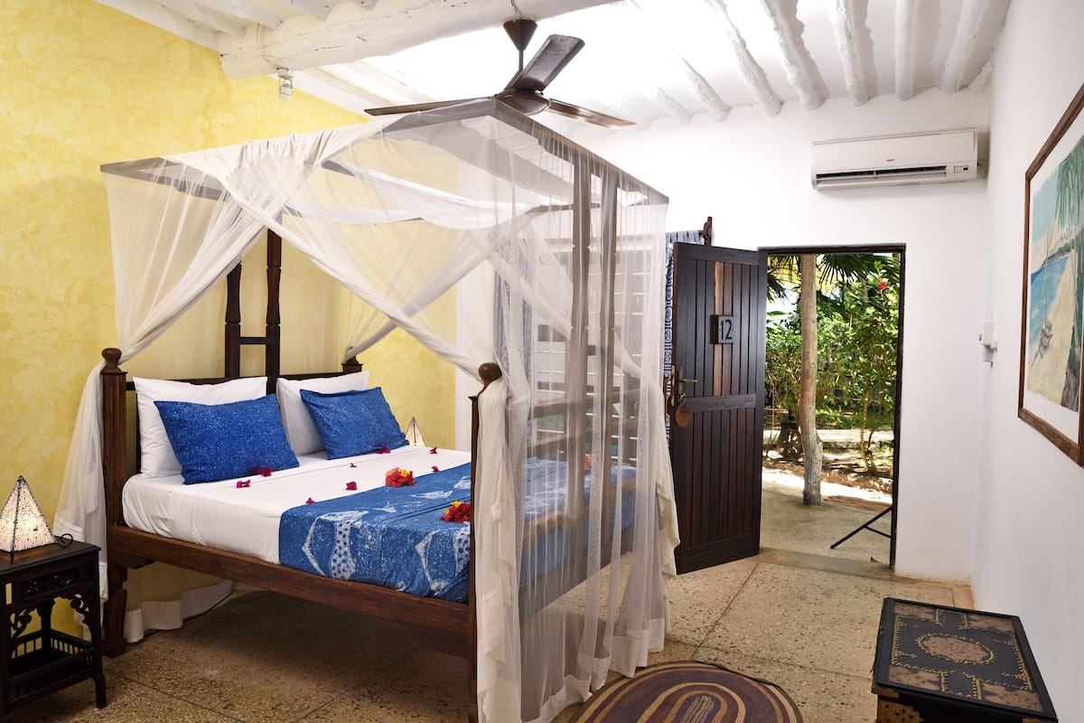 Un dormitorio con una cama bajo una mosquitera, un ventilador de techo y una puerta que da a un espacio exterior.