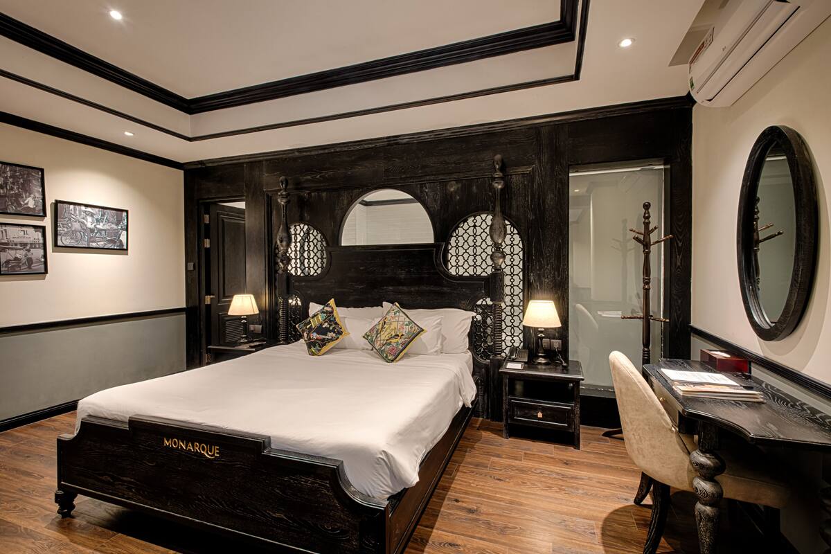 A hotel room with a large bed, two bedside tables, a desk with a chair, a large mirror, and a wardrobe.