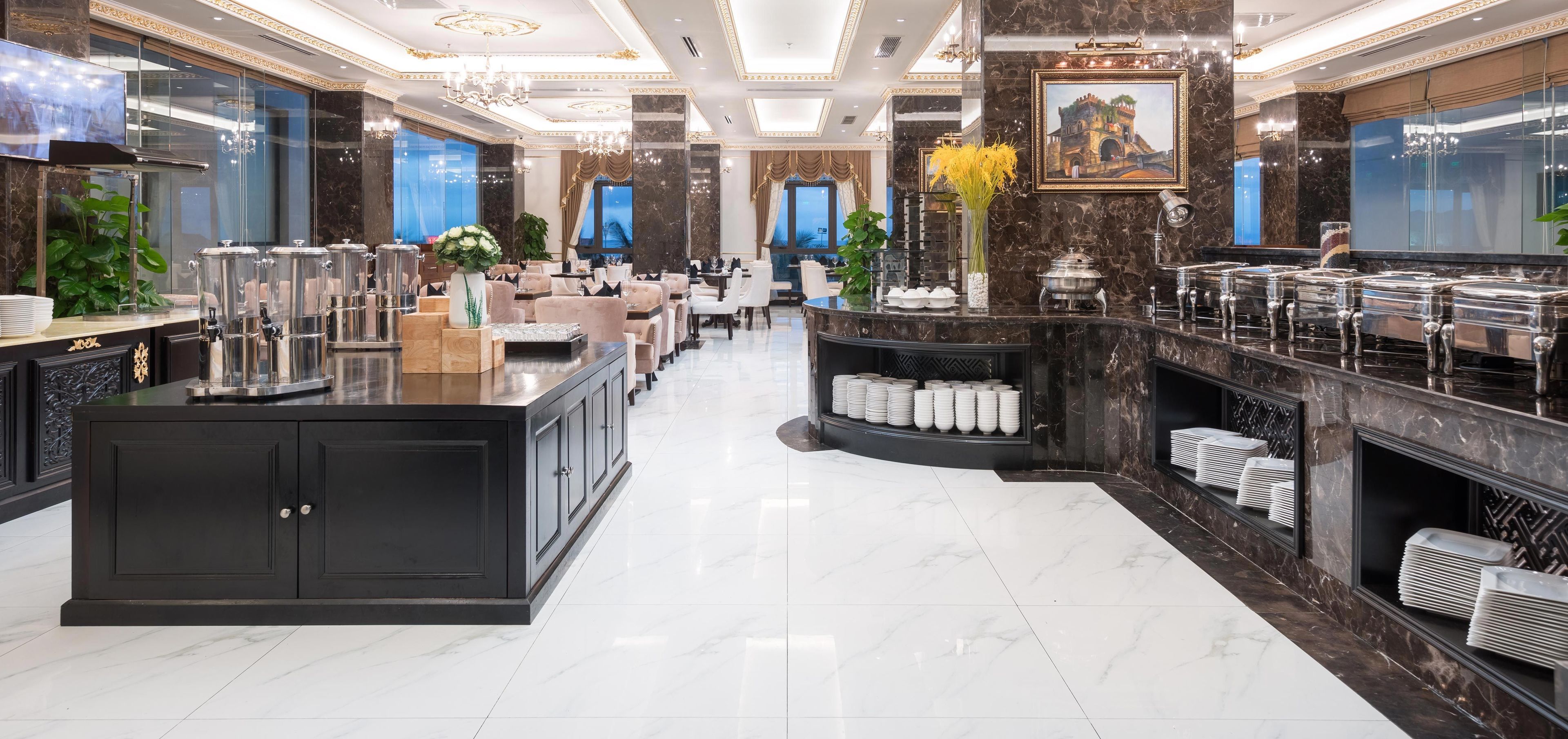 A spacious hotel lobby with a marble floor, a central reception desk, and a dining area with tables and chairs.
