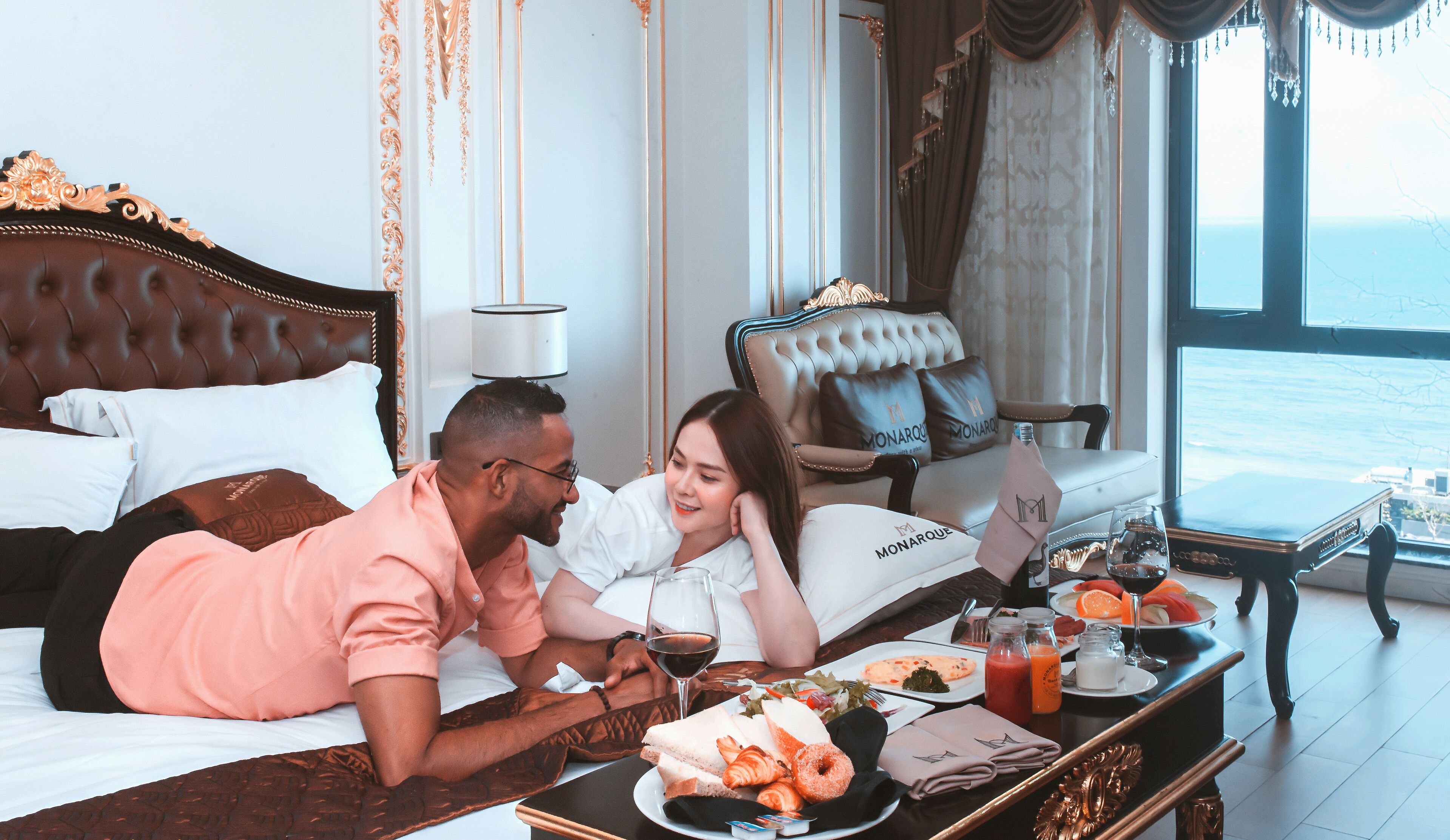 Um quarto luxuoso com uma cama king size, um espaço de estar com um sofá e uma mesa de jantar com itens de café da manhã.