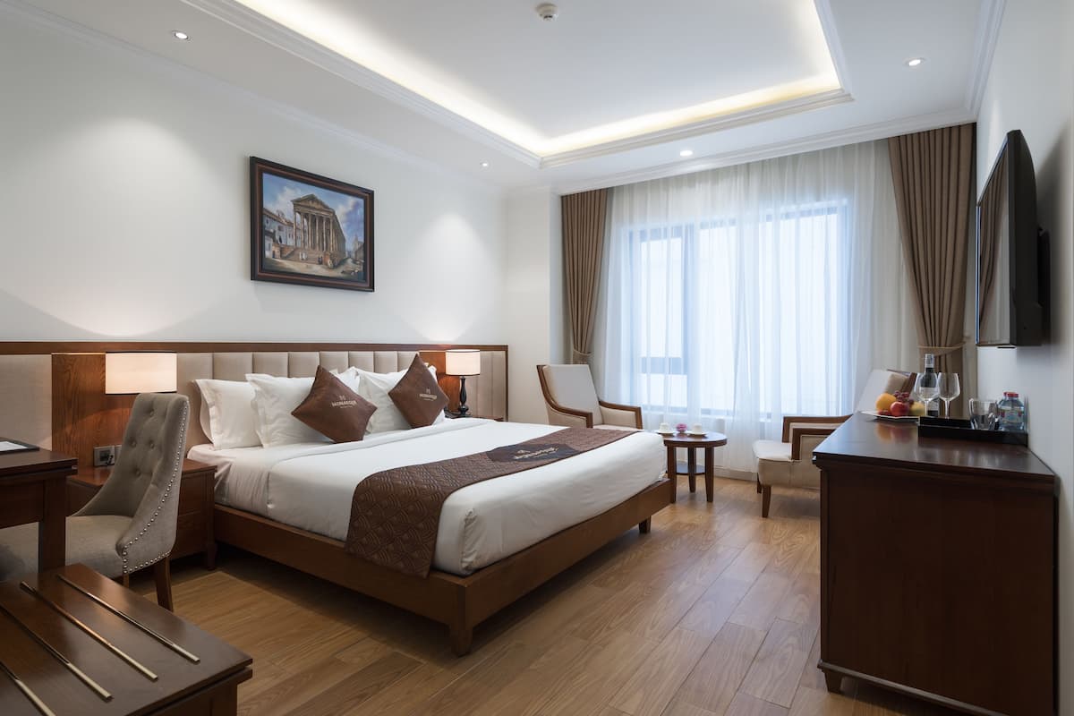 A hotel room with a large bed, a desk, a chair, a TV, and a window with curtains.