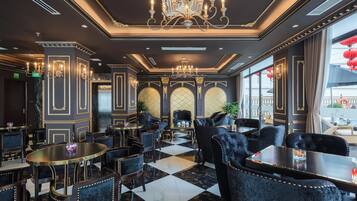 A luxurious dining area with marble flooring, elegant black upholstered chairs, and chandeliers.