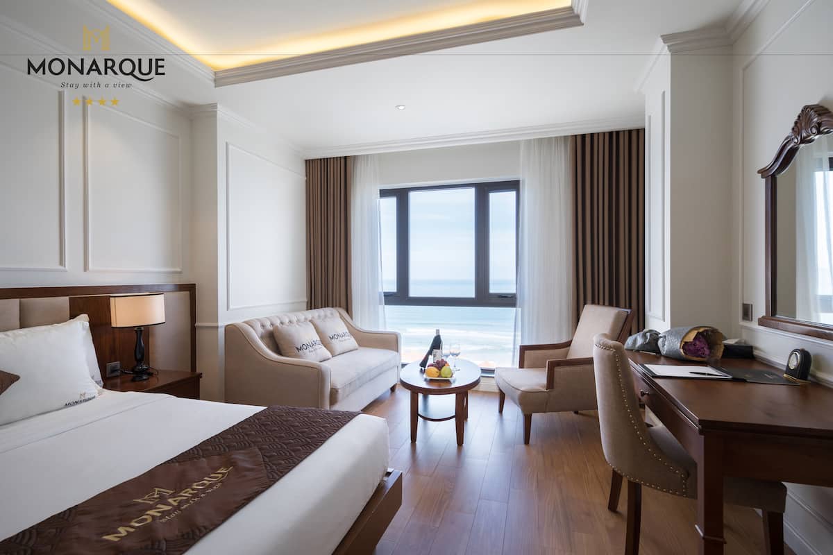 A hotel room with a bed, a sofa, a desk, a chair, and a view of the ocean.