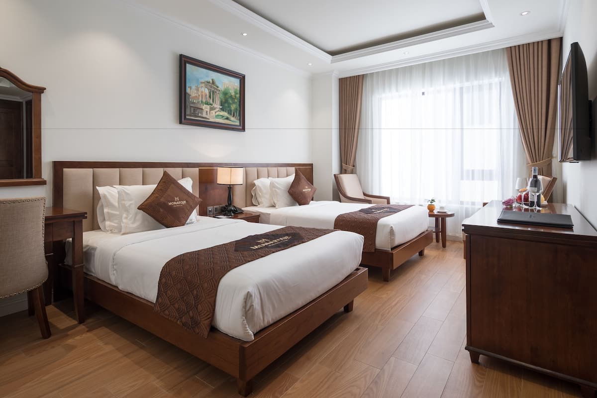 A hotel room with two beds, a desk, a chair, a TV, and a painting on the wall.