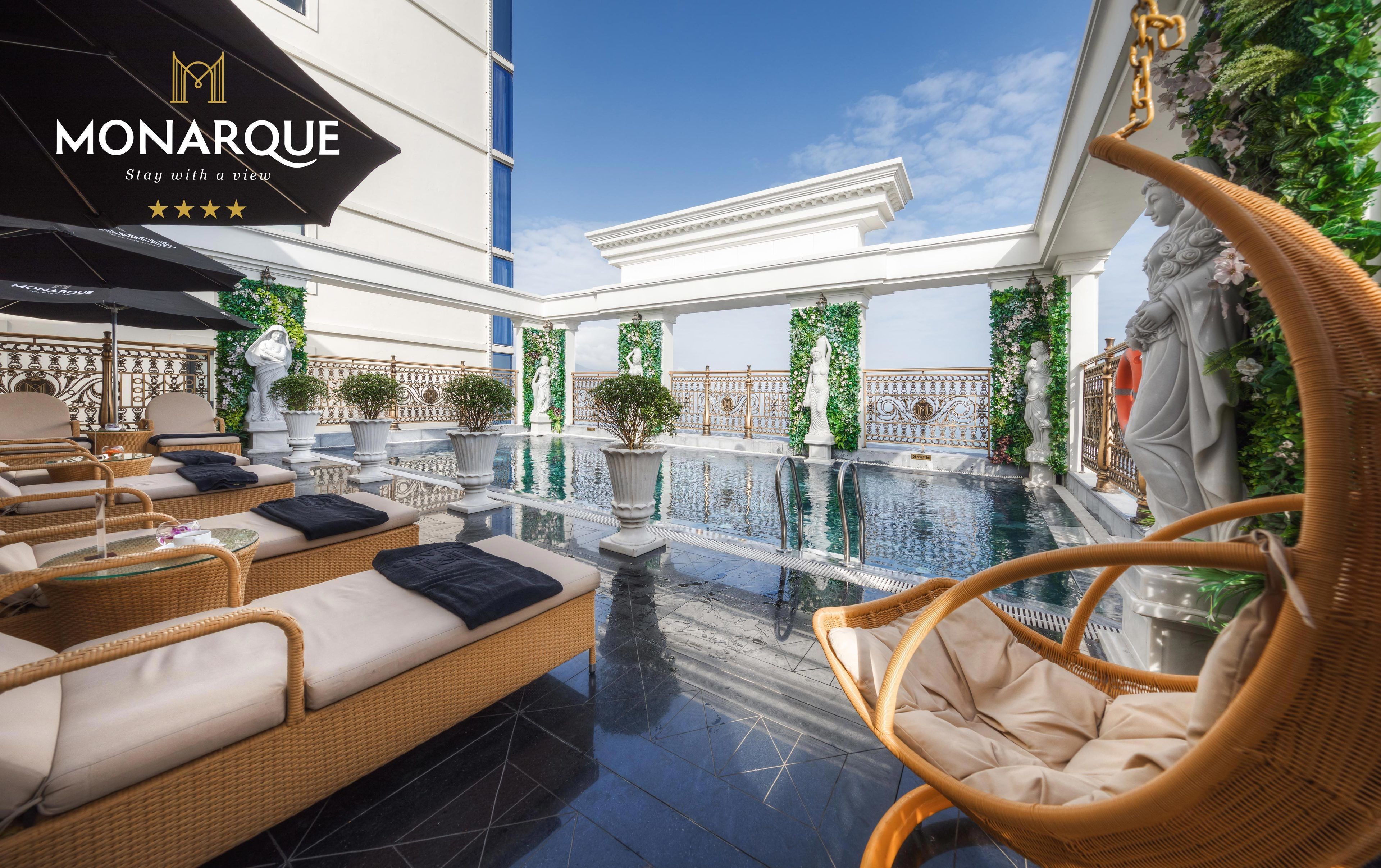 A luxurious outdoor pool area with wicker furniture and statues, surrounded by ornate railings and greenery.