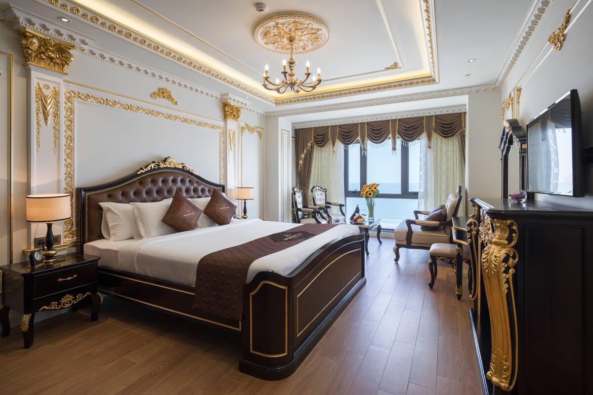 A luxurious bedroom with a large bed, ornate ceiling, and a television.