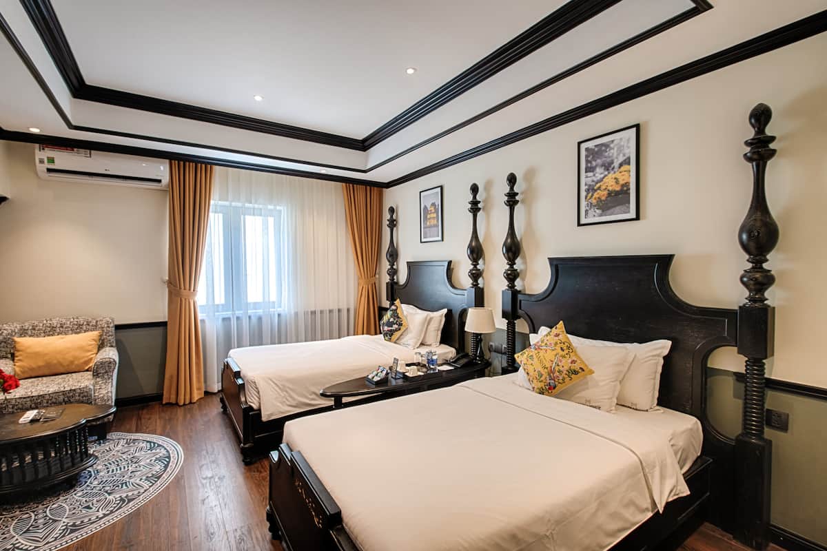 A hotel room with two beds, a sofa, a round coffee table, and a large window with curtains.