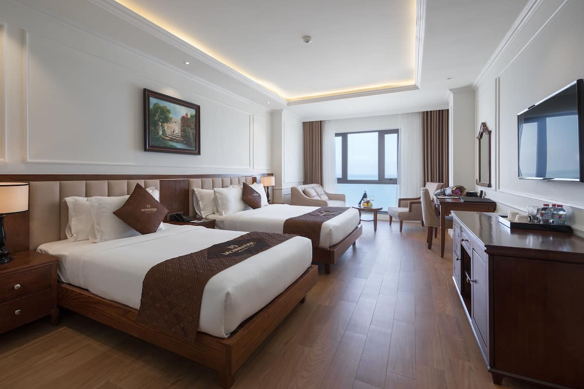 A hotel room with two beds, a desk, a chair, a TV, and a painting on the wall.