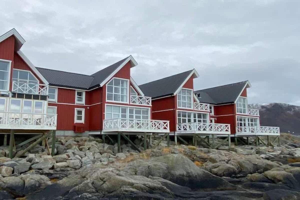 A row of red wooden houses with white railings, built on stilts over rocky terrain.