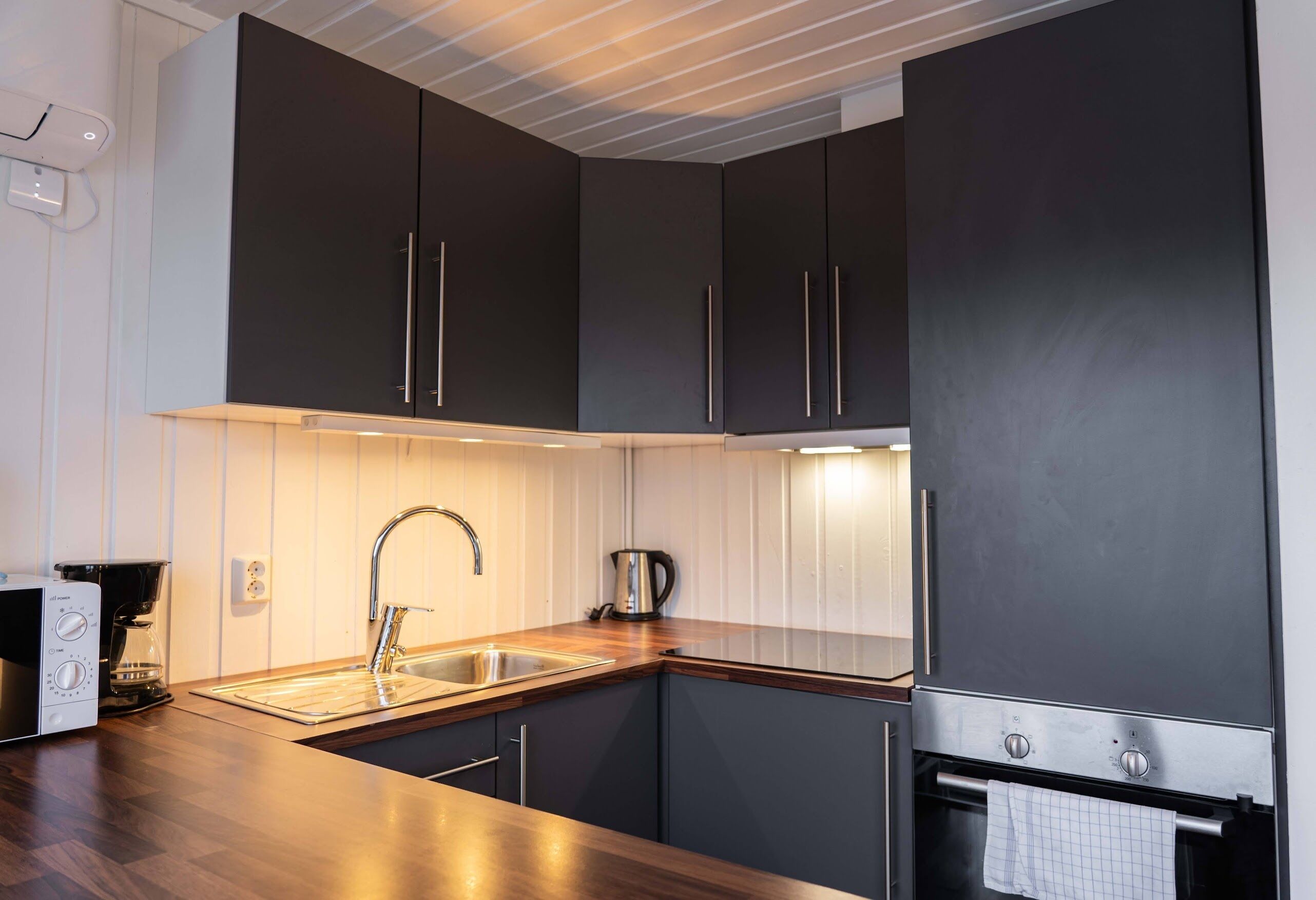 A modern kitchen with dark cabinets, a stainless steel sink, and a built-in oven.
