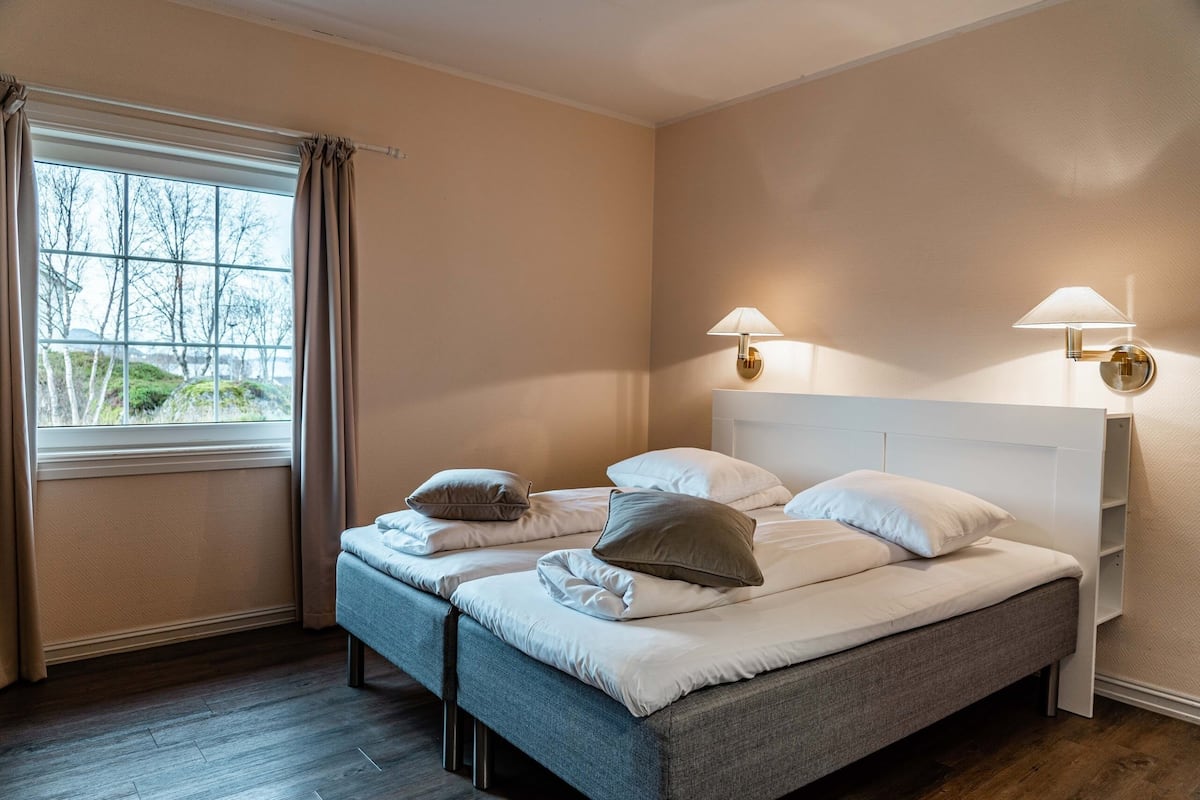 A bedroom with two beds, a window with curtains, and wall-mounted lamps.
