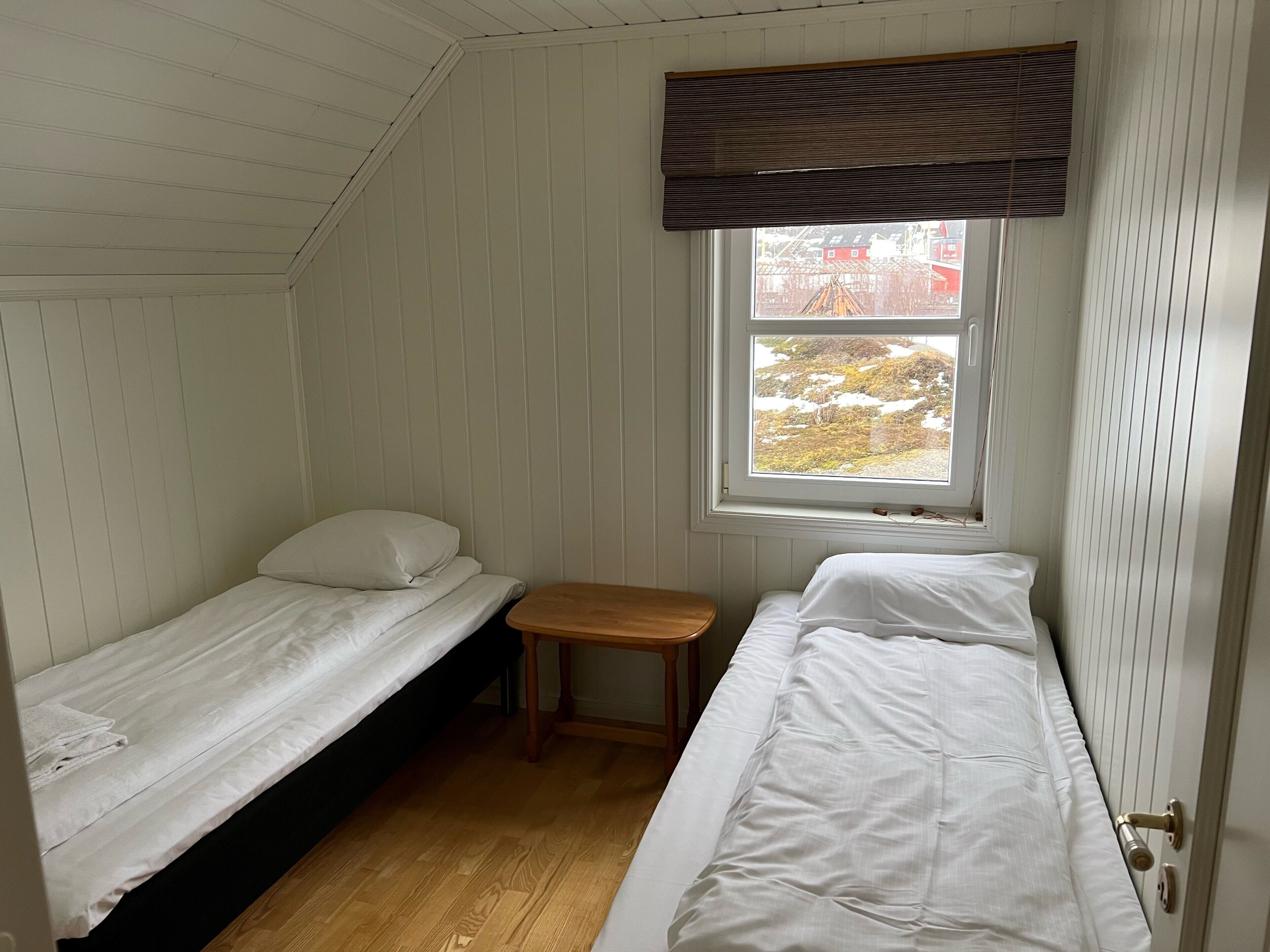 Una cabaña pequeña de una sola habitación con dos literas, un banco de madera y una ventana con vistas a un paisaje nevado.