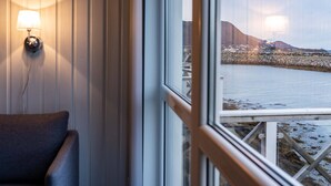 Ein Zimmer mit Blick auf eine felsige Küste und einen Berg in der Ferne durch ein Fenster.