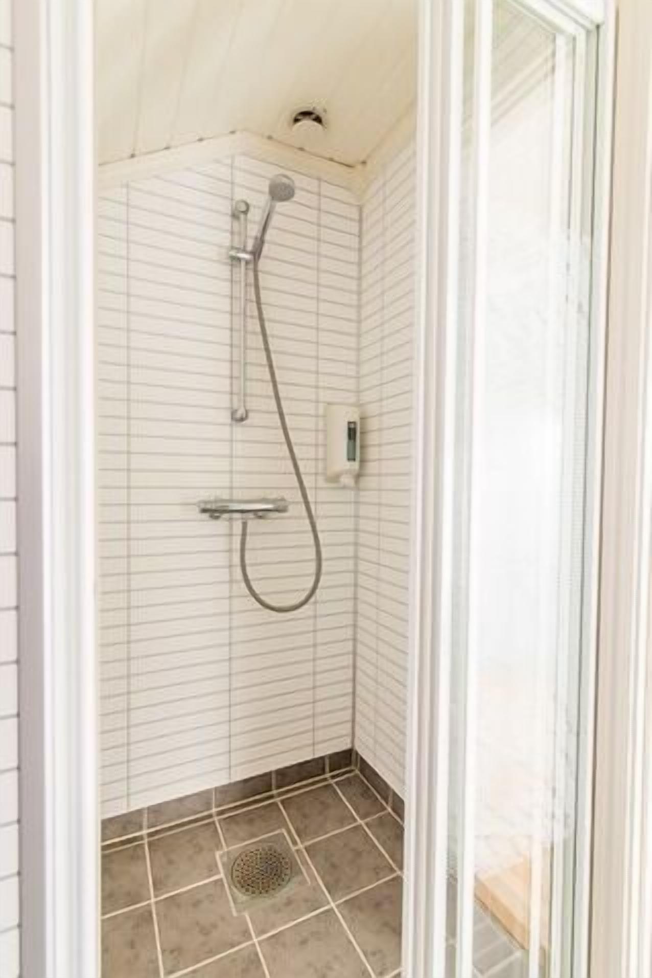 Un espacio de ducha pequeño y cerrado, con paredes y suelo de azulejos, un cabezal de ducha de mano y un grifo empotrado.