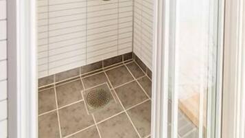 Un espacio de ducha pequeño y cerrado, con paredes y suelo de azulejos, un cabezal de ducha de mano y un grifo empotrado.