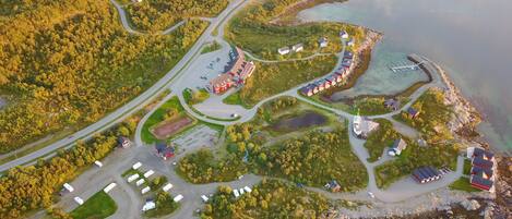 Vue aérienne d’une zone côtière comprenant un port de plaisance, un réseau routier et plusieurs bâtiments, dont une grande structure rouge et des maisons plus petites.