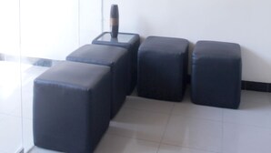 A modern waiting area with a glass partition, a metal light fixture, and four black cushioned seating areas. - Citra Suites Surabaya (Surabaya)