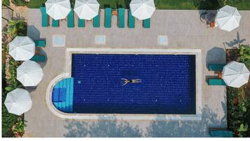 Vista aérea de una piscina rectangular con una persona nadando, rodeada de sillas de descanso y sombrillas.