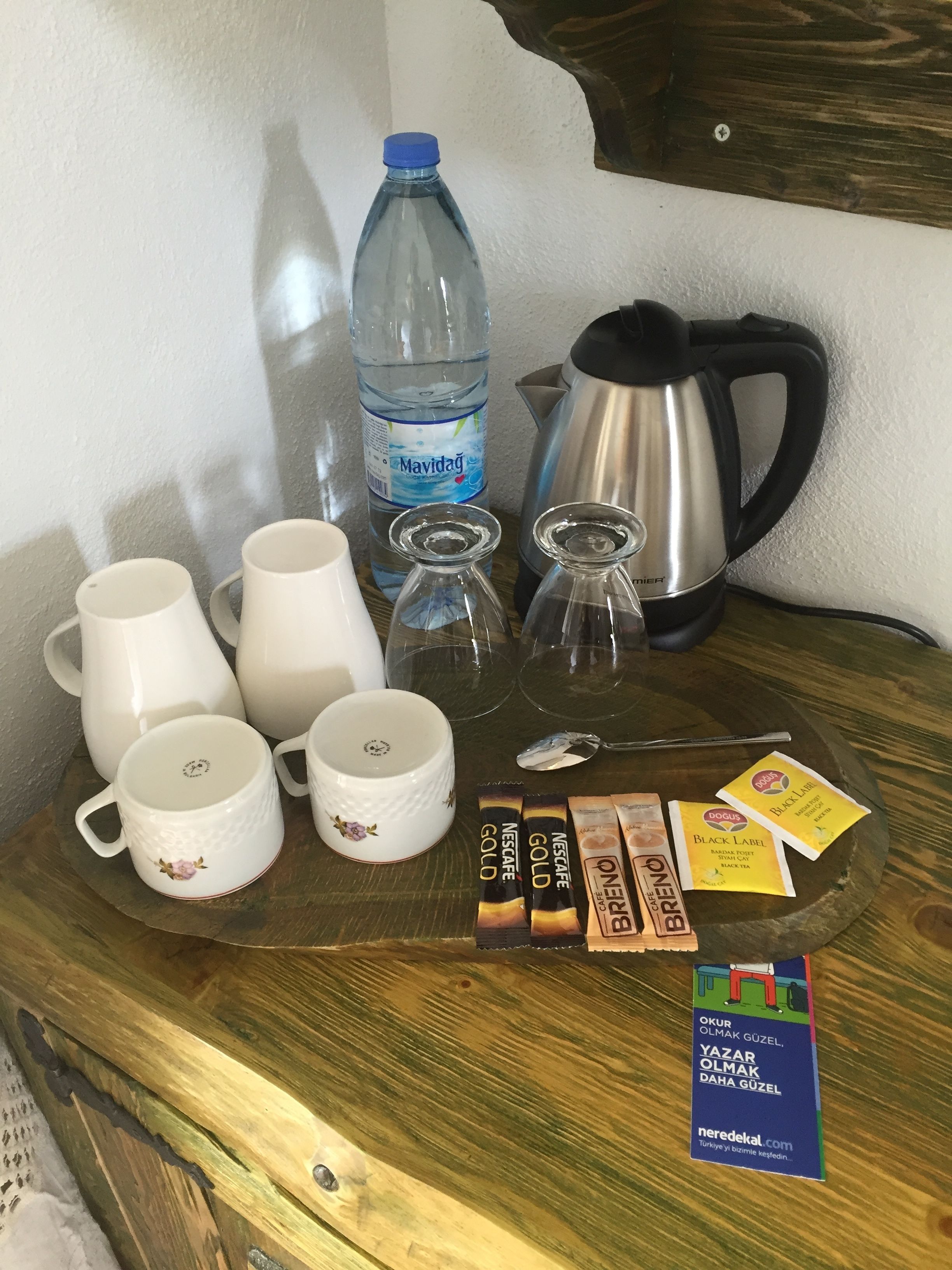 Una bandeja con tazas de café, una botella de agua, una cafetera y sobres de café sobre una superficie de madera.