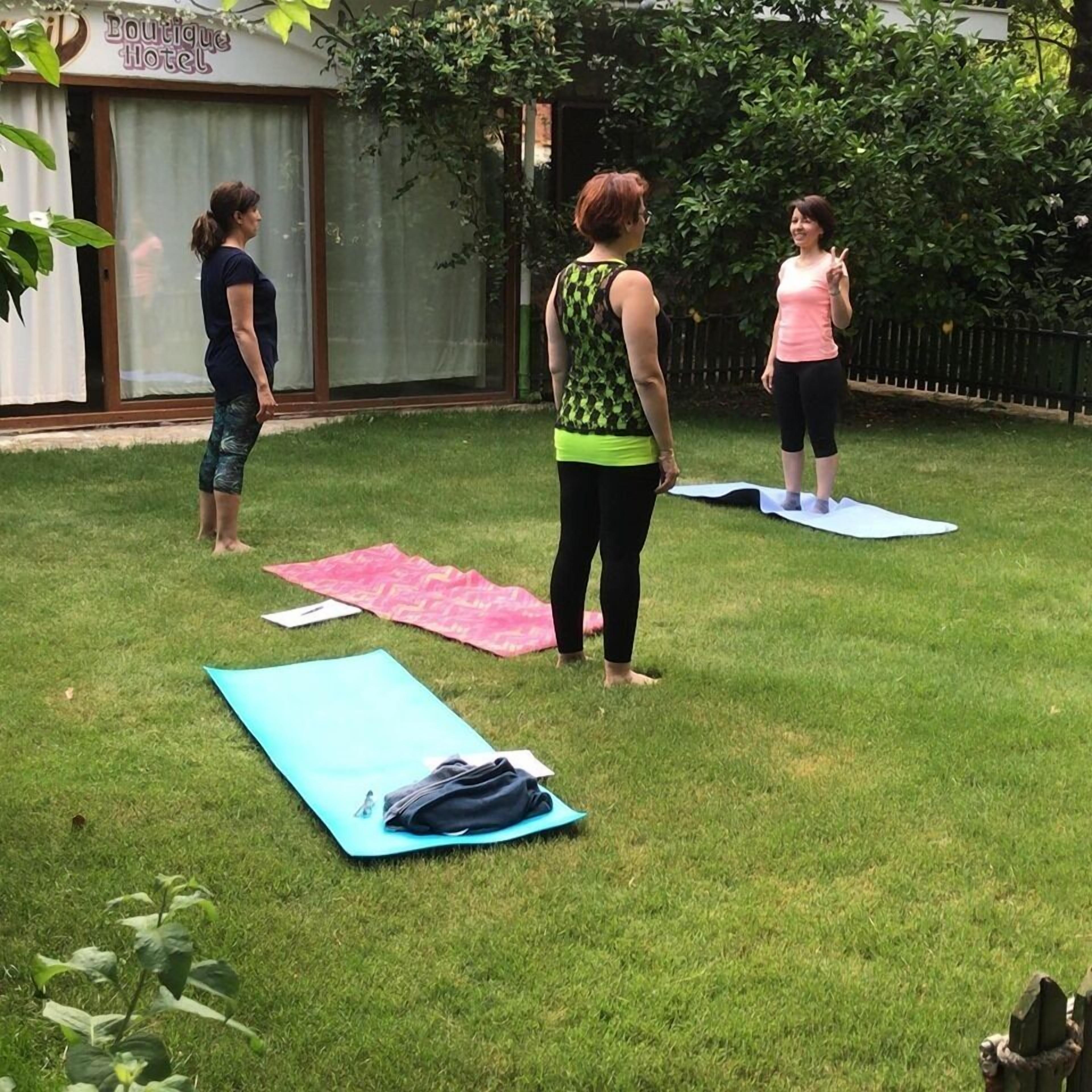 Un espacio al aire libre con un cartel de Boutique Hotel, tres personas sobre esterillas de yoga y un césped.