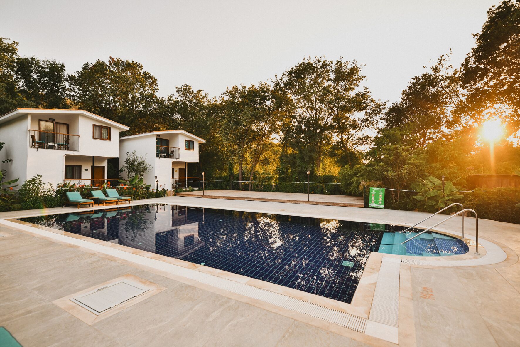 Una piscina con cubierta de baldosas, sillas de descanso y un edificio con balcones al fondo.