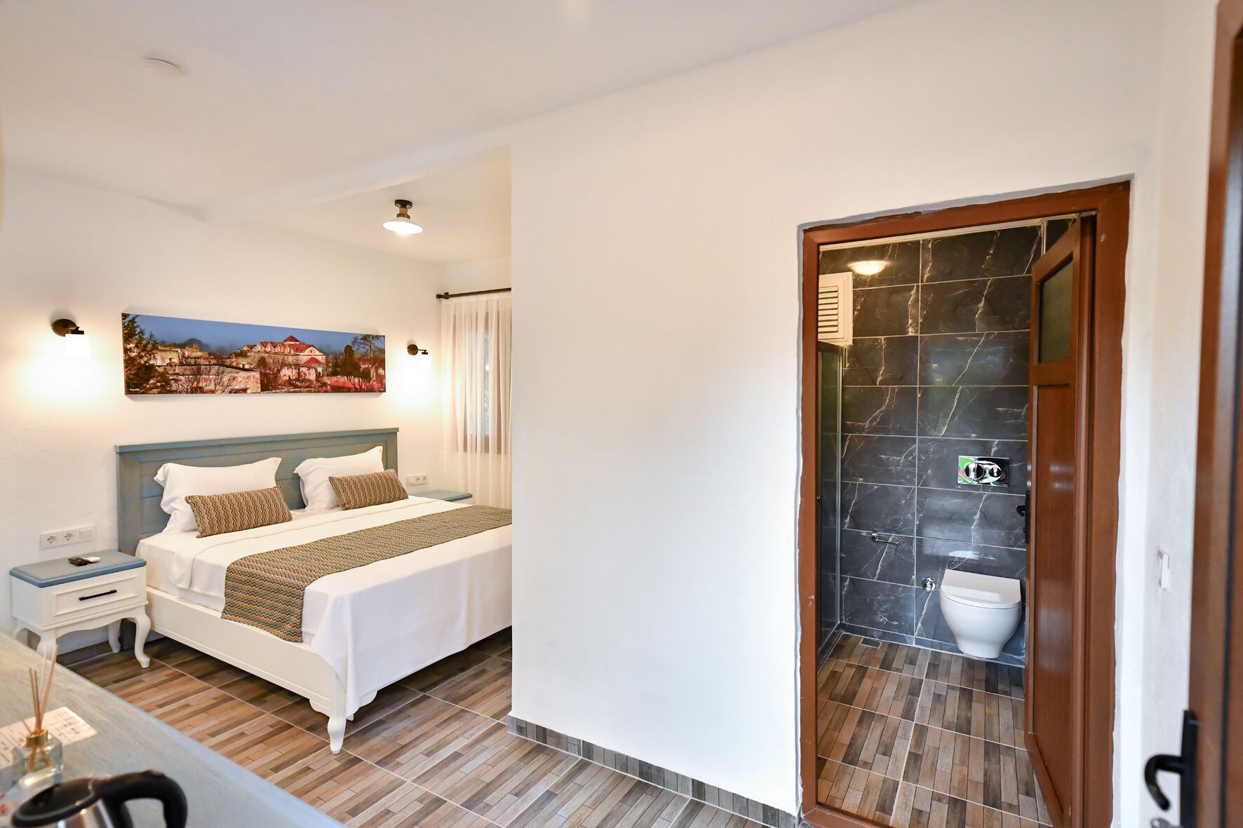 A bedroom with a bed, bedside table, and a painting on the wall.