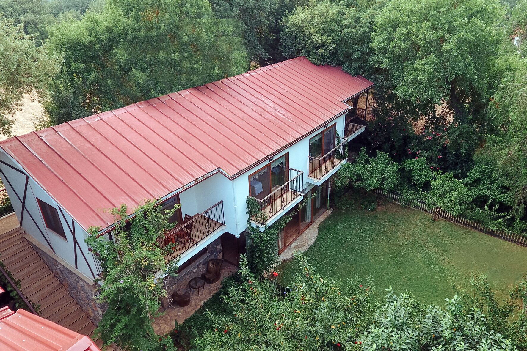 A two-story house with a red roof, surrounded by lush greenery and a fenced yard.