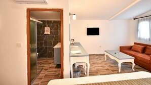 A hotel room with a bed, a seating area with a table, a TV, and a bathroom visible through an open door. - Piramit Hotel (Fethiye)