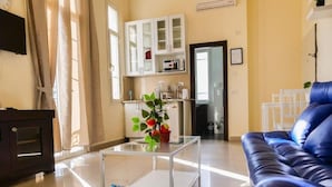 A living room with a blue sofa, a glass coffee table, and a white cabinet with kitchen appliances. - TLV Urban Life Style (Tel Aviv)