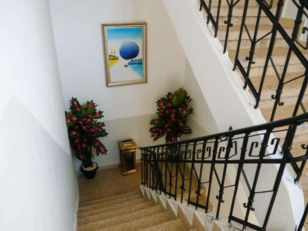 Un escalier avec des rampes en métal noir, des plantes en pot ornées de fleurs roses et une œuvre d’art encadrée accrochée au mur.