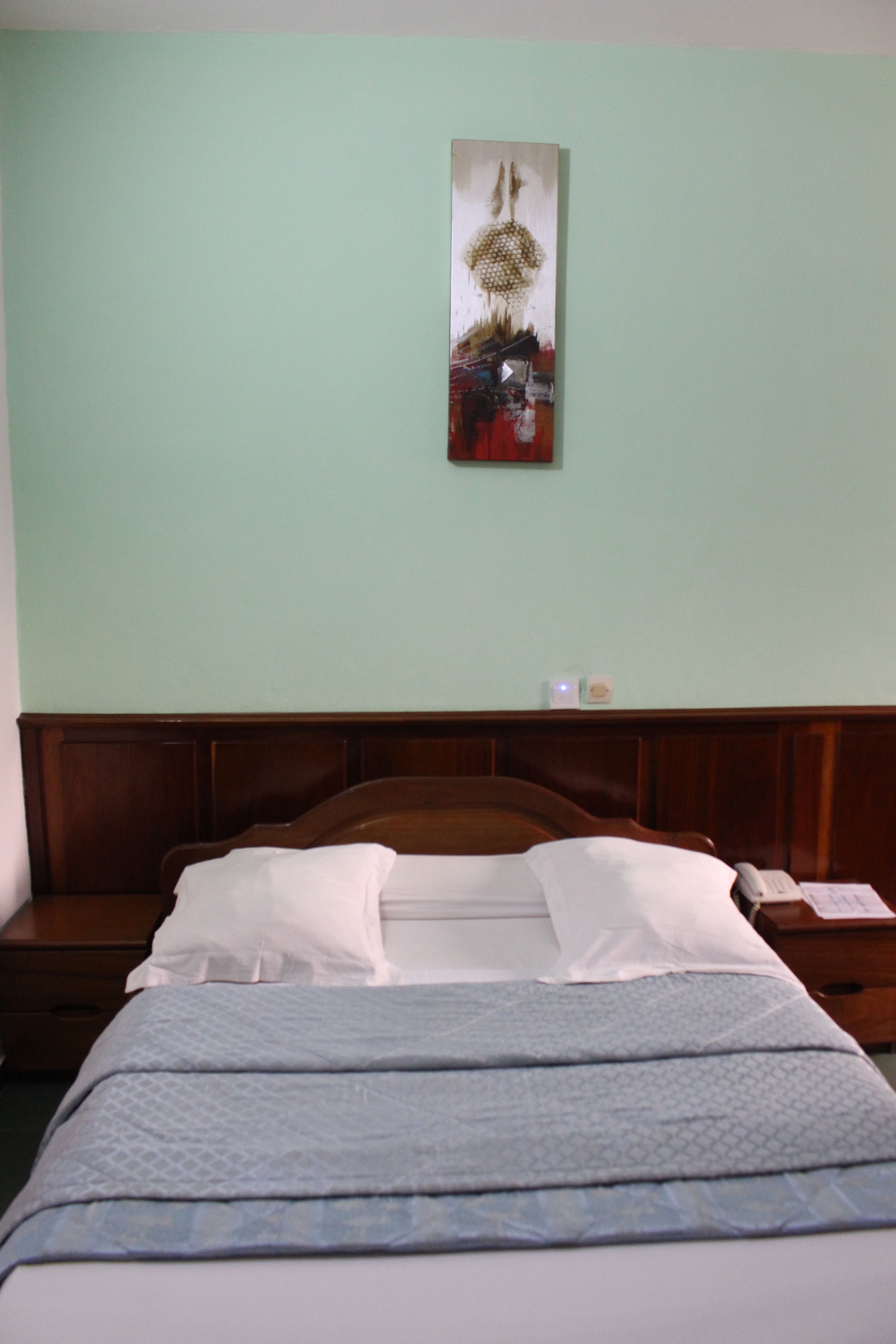 Habitación de hotel con cabecera de madera, cama con ropa blanca y una obra de arte colgada en la pared.