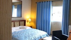 A hotel room with a bed, a chair, a desk, a lamp, and a window with curtains. - Jet Hôtel (Douala)