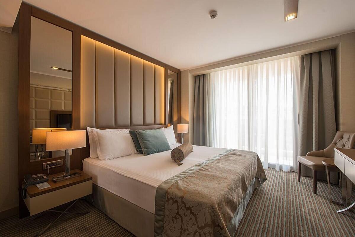 A hotel room with a large bed, a desk, a chair, a mirror, and a window with curtains.