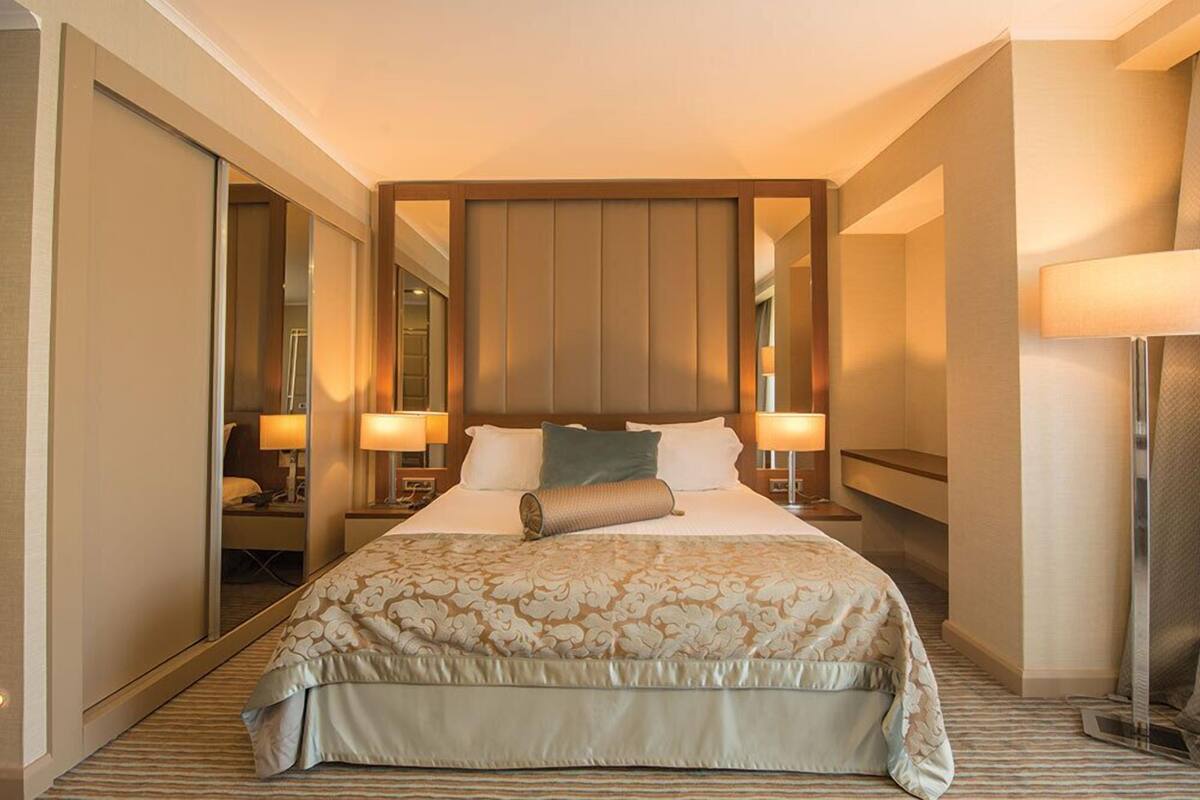 A hotel room with a large bed, two bedside lamps, a mirror, and a view of the hallway.