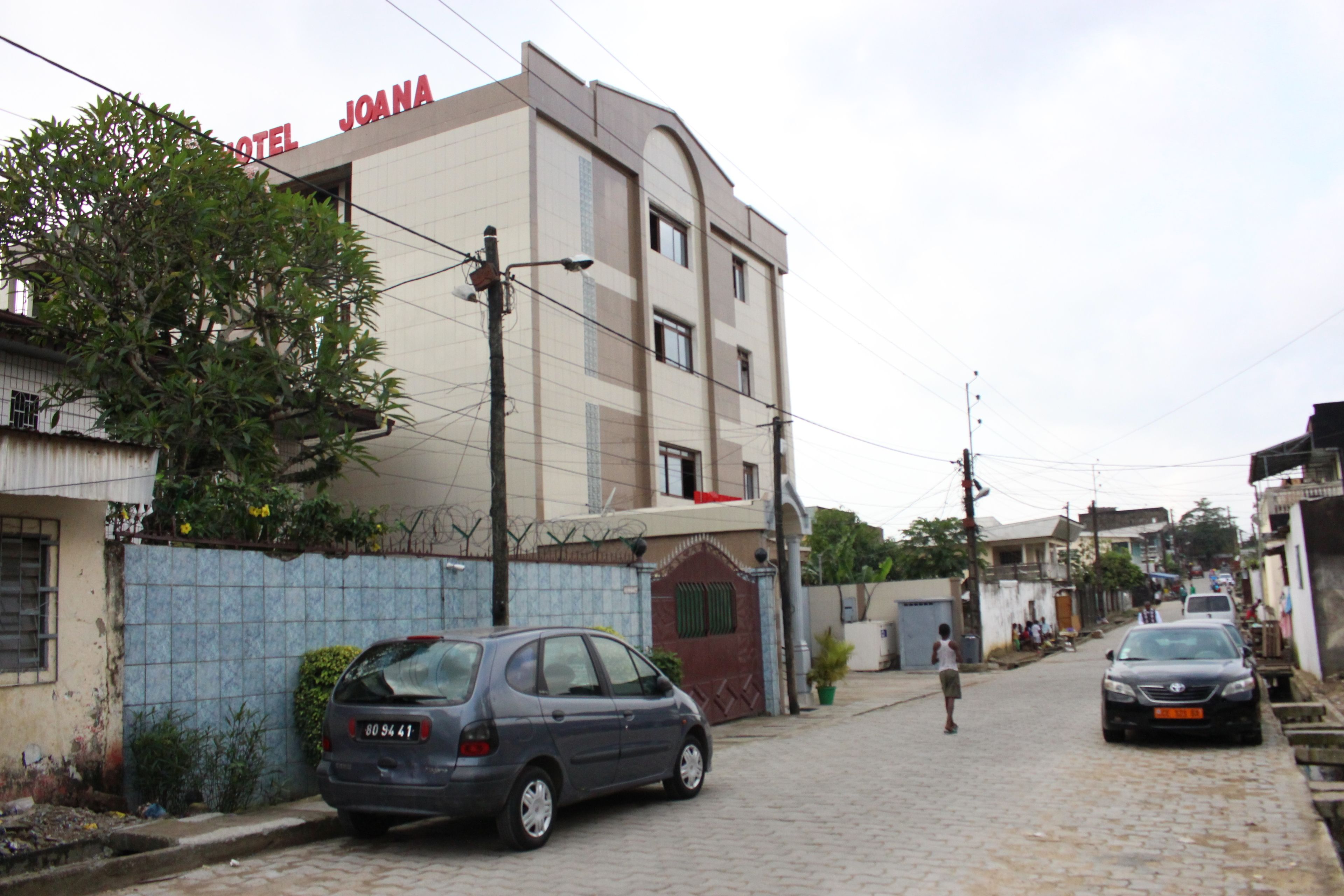 A hotel named "HOTEL JOANA" with a tiled facade, a parked car, and a cobblestone street.