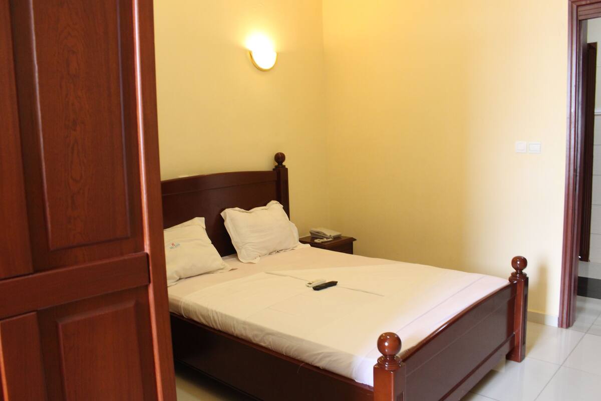 A neatly made bed with a wooden headboard, a bedside table with a lamp, and a wall-mounted light fixture.