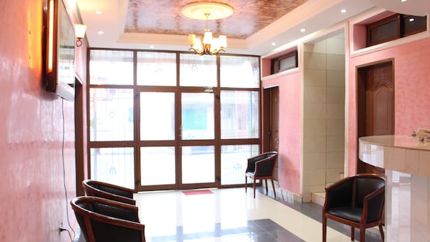 A hotel lobby with a large glass door, a chandelier, and several wooden chairs. - Hotel Joana (Douala)