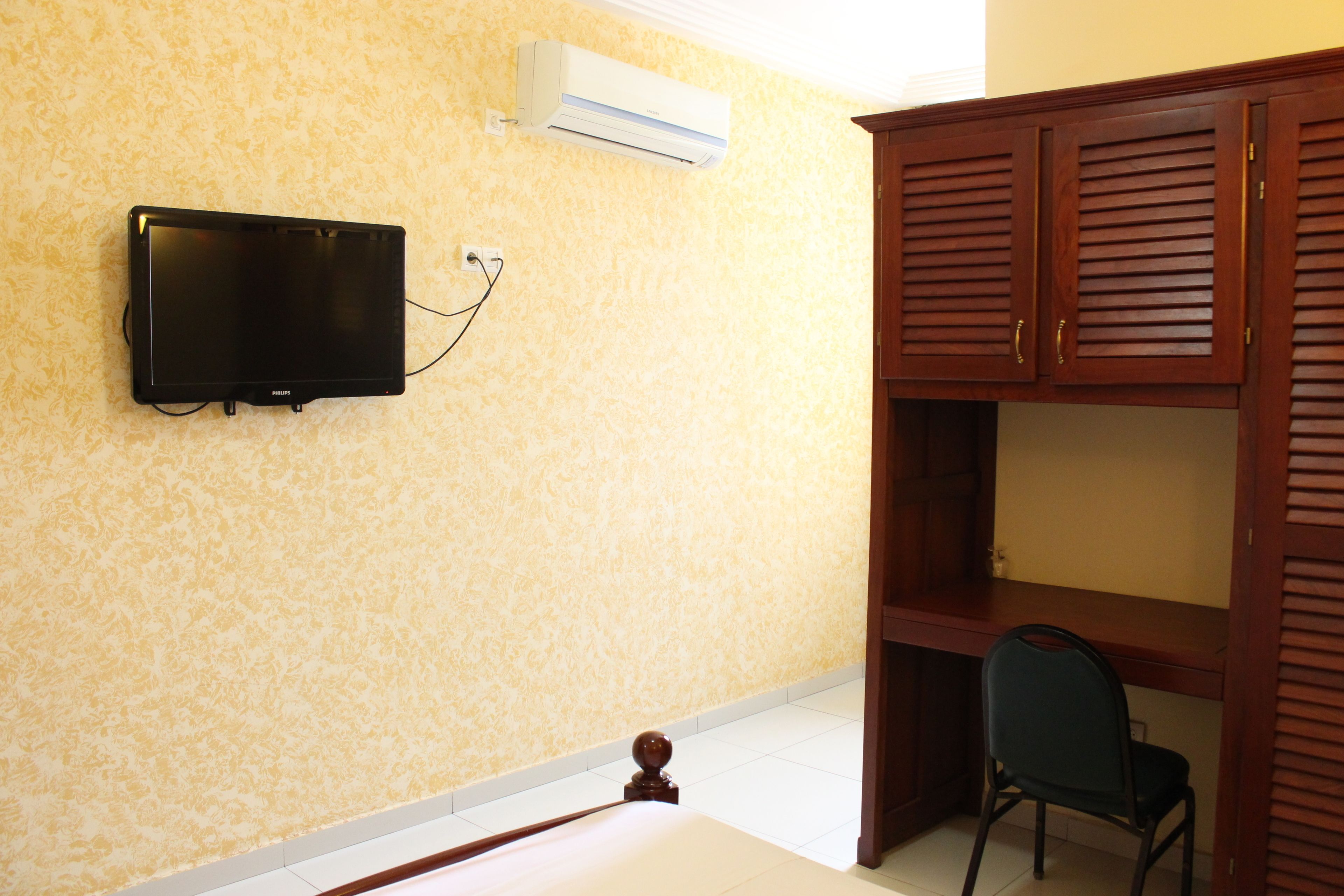 Una habitación con una televisión de pantalla plana montada en la pared, un armario de madera y una silla.