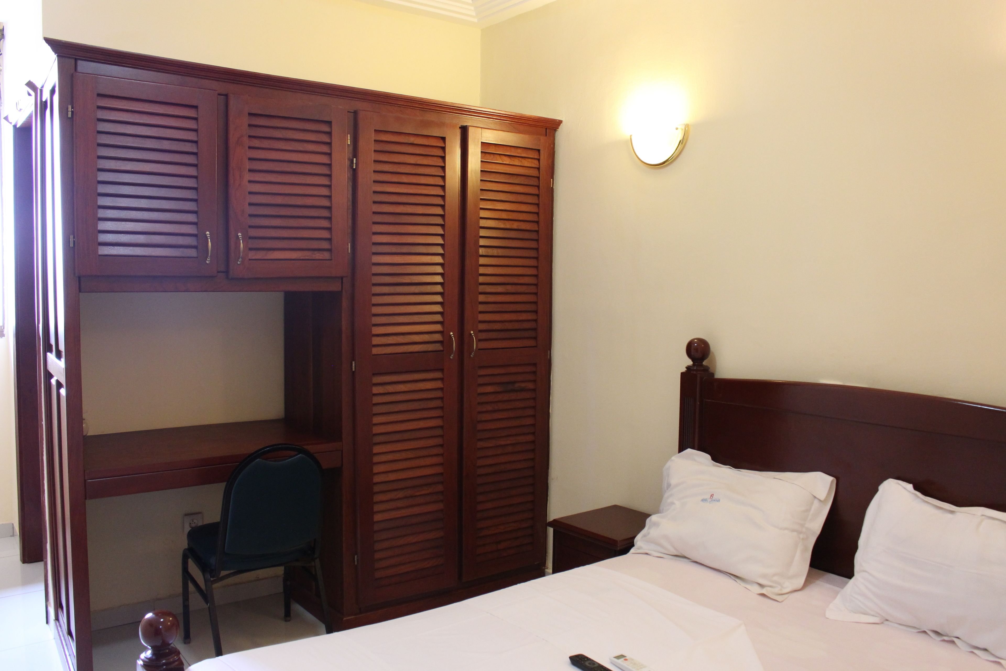 Un dormitorio con cama, almohadas blancas, un escritorio con silla y un armario.