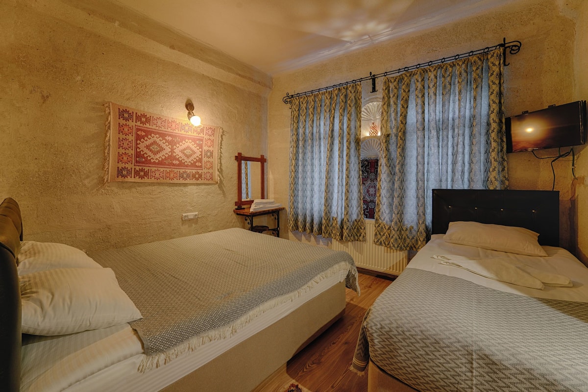 Una habitación con dos camas, un televisor de pared, una alfombra estampada y una ventana con cortinas.